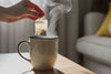 a woman dipping a tea bag in a steaming mug.
